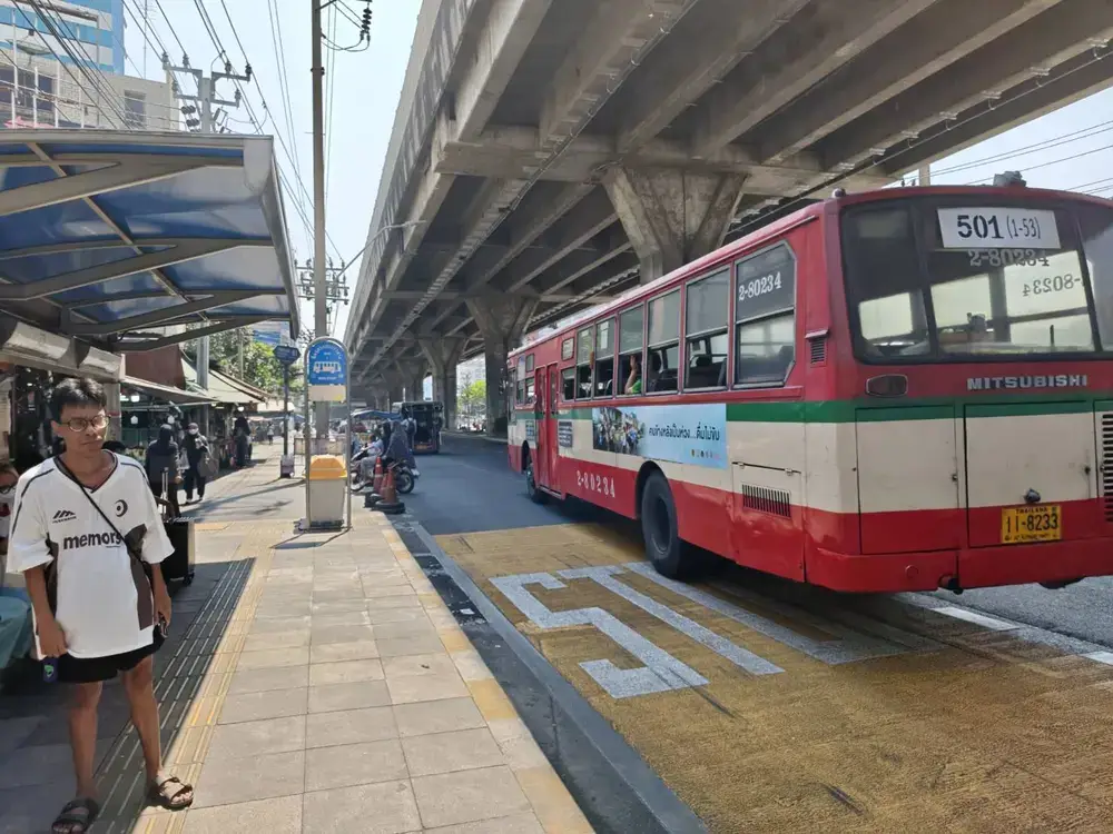 バンコクの街中を走る赤バスとFBTスポーツコンプレックス前の歩道