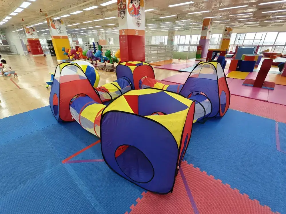カラフルなトンネル遊具とクッションマットが敷かれた遊び場